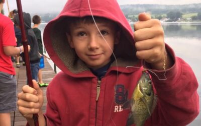 Cub Scout in hoodie holding up a sunfish he just caught