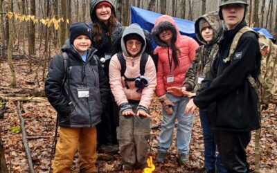 Three female and three male Scouts around a campfire in the woods