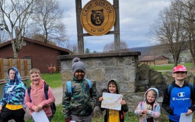 6 Cub Scout boy and girl members with maps in front of the sign for Camp Gorton