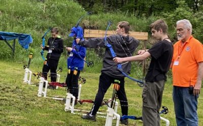 Four Scouts practice archery, guided by an adult volunteer