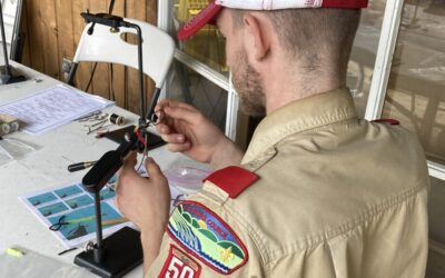 A member of Scout Troop 50 in uniform ties a fishing fly at the Big Horn Camporee 2024