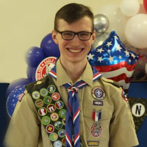 smiling Eagle Scout in uniform in front of red, white, blue, and American flag-inscribed balloons